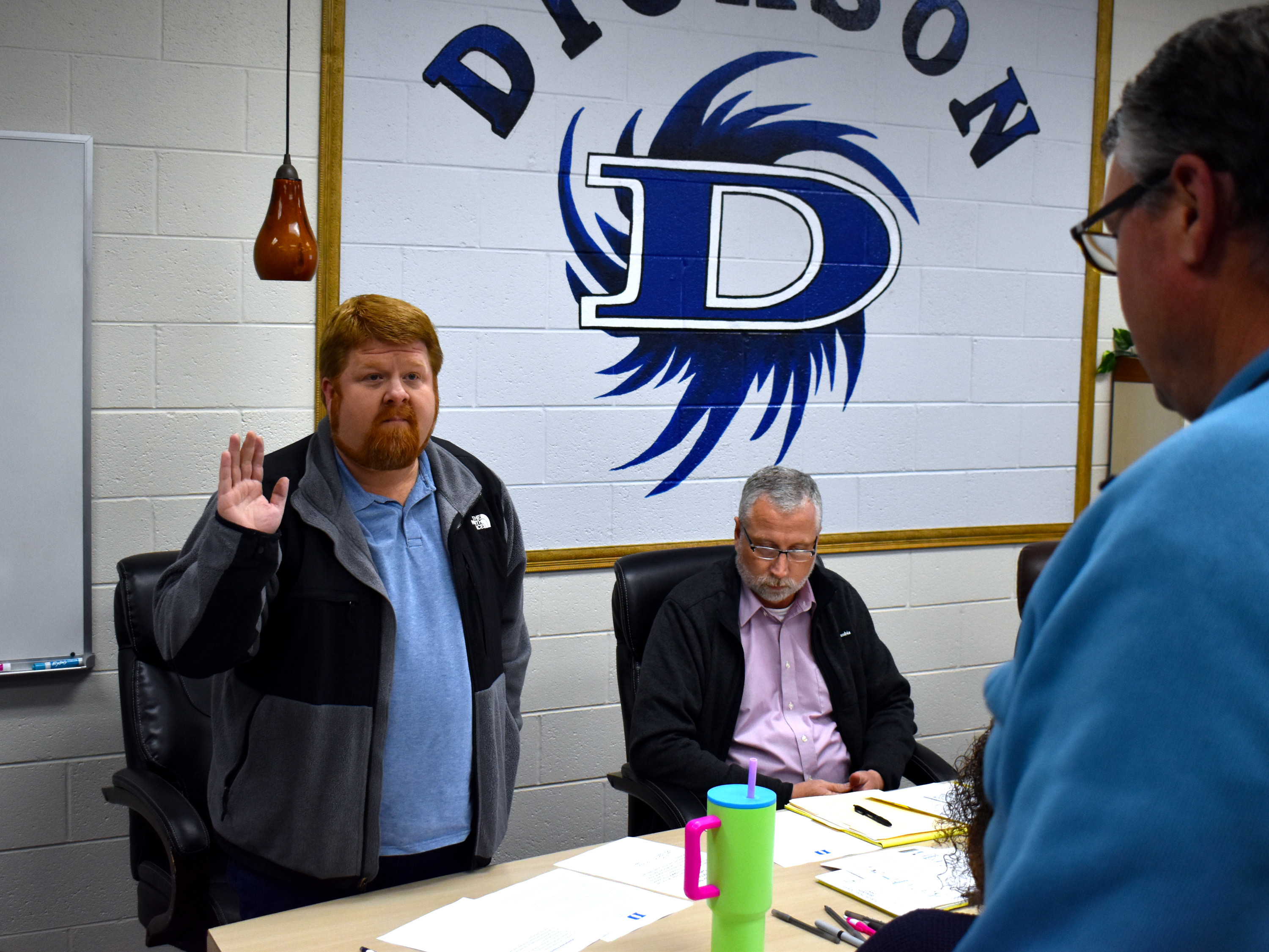 Jacob Tynes raises his right had to take the oath of office in front of fellow board members and school officials, including Superintendent Jamie Mitchell seated.